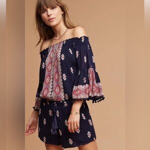Anthropologie Lilka romper with tassel tie waist & pom-trimmed swing sleeves.